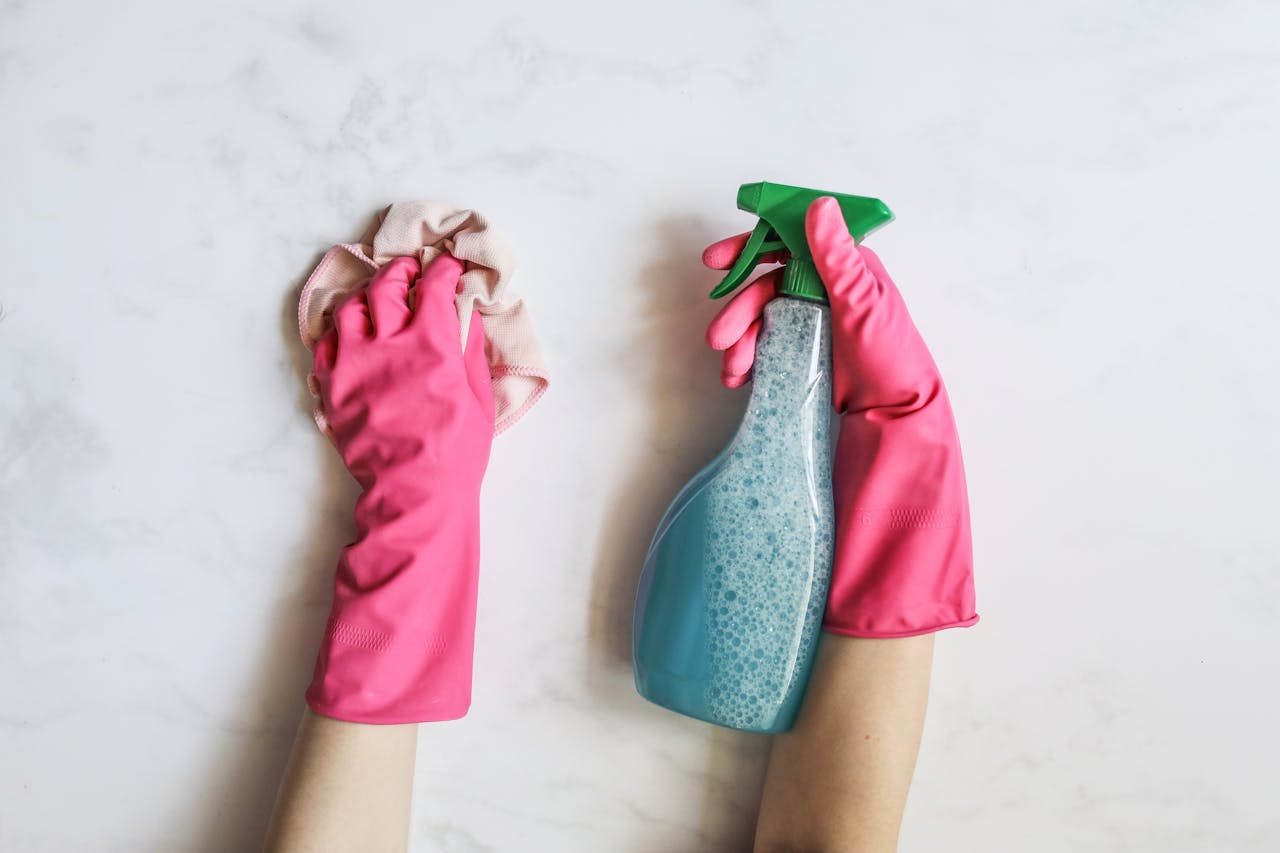 services-03 A pair of hands in pink gloves are cleaning with a spray bottle on a white background.